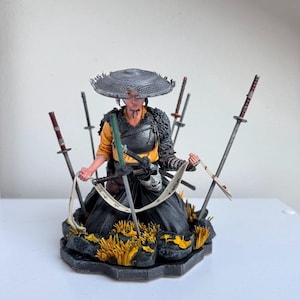 以下が含まれることがあります： 麦わら帽子と黒い衣装の戦士の精巧なフィギュア。剣に囲まれています。 決意した表情でポーズをとっており、黄色のアクセントが付いた岩の台座に置かれています。 剣は長さと色が異なります。