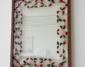 May include: A rectangular wall mirror with a wooden frame featuring a decorative border of painted strawberries, green leaves, and white flowers on a clear glass background with a red and white checkered pattern along the inner edge.