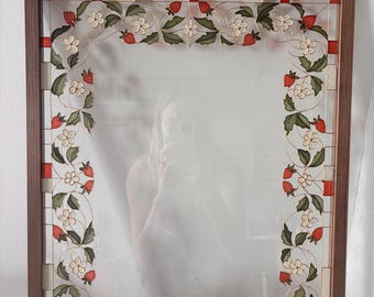 May include: A rectangular mirror framed in brown wood featuring a decorative border of painted strawberries, green leaves, and white flowers. The design is outlined in thin gold lines, with small red and cream-colored squares along the outer edge.