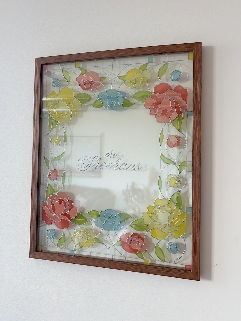 May include: A framed floral artwork featuring a brown wooden frame. The artwork showcases colorful flowers in shades of red, yellow, and blue, with the text "the Sheehans" in the center.