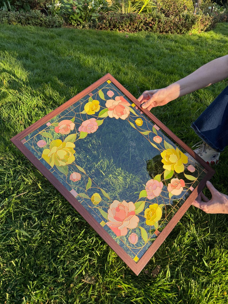 May include: A square decorative mirror with a dark blue background and a floral design. The flowers are in shades of yellow and pink, with green leaves and gold accents. The frame is a dark brown color.