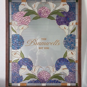 May include: A rectangular mirror framed in dark wood, featuring a decorative stained glass border of pink and blue hydrangea clusters and white calla lilies. The center of the mirror displays the gold text "THE Brumwells EST 1990".