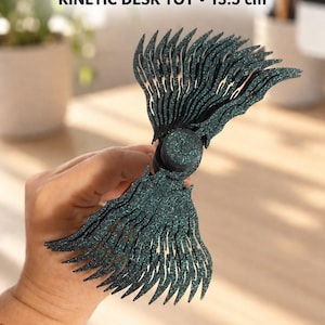 Può includere: Un fidget star spinner cinetico da scrivania di colore verde scuro glitterato, dotato di un perno centrale circolare e di numerose lame sovrapposte a forma di ala. Il testo FIDGET STAR SPINNER KINETIC DESK TOY 13.5 cm è stampato sopra.
