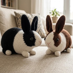 May include: Two handmade crochet bunny rabbits. One is black and white, the other is brown and white. Both have button eyes and pink noses. They are sitting on a beige couch.