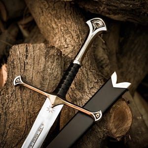 May include: A silver-toned metal sword with a black leather-wrapped grip, a crossguard featuring triangular engravings, and a pommel with matching details. The blade displays an etched star symbol and runic inscriptions, accompanied by a black scabbard.