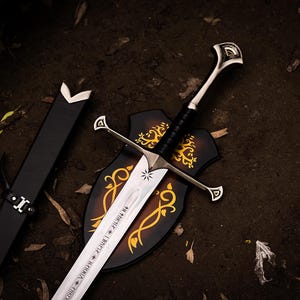 Peut inclure: Une épée en métal argenté avec une poignée gainée de cuir noir, une garde à accents triangulaires et une lame gravée d'inscriptions runiques et d'un symbole d'étoile. Elle est accompagnée d'un fourreau noir et d'une plaque murale en bois.
