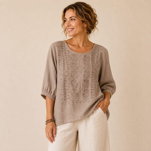 Op de afbeelding: Een taupekleurige blouse met driekwartmouwen en een ronde halslijn. Het voorpand is versierd met verticale rijen ton-sur-ton bloemenborduursels en geschulpte details. Het kledingstuk wordt gecombineerd met een lichtbeige broek.