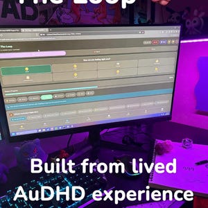 May include: A computer monitor displaying a website interface with the text "The Loop" and "Built from lived AuDHD experience." A keyboard, mouse, and notebook are visible. The scene is illuminated with purple and blue lighting.