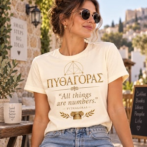 Può includere: Una t-shirt a maniche corte color crema con una stampa grafica dorata. Il design include il testo greco ΠΥΘΑΓΟΡΑΣ, un simbolo geometrico, la citazione "All things are numbers", il nome "Pythagoras" e un'illustrazione di una colonna.