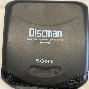 May include: A black Sony Discman CD compact player. The device has the word "Discman" printed in white, along with "MEGA BASS" and other text. The Sony logo is also visible.