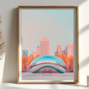 May include: A framed art print featuring a cityscape with a large, reflective, bean-shaped sculpture in the foreground. The buildings are in shades of pink and orange, with a blue sky. The print is in a wooden frame.