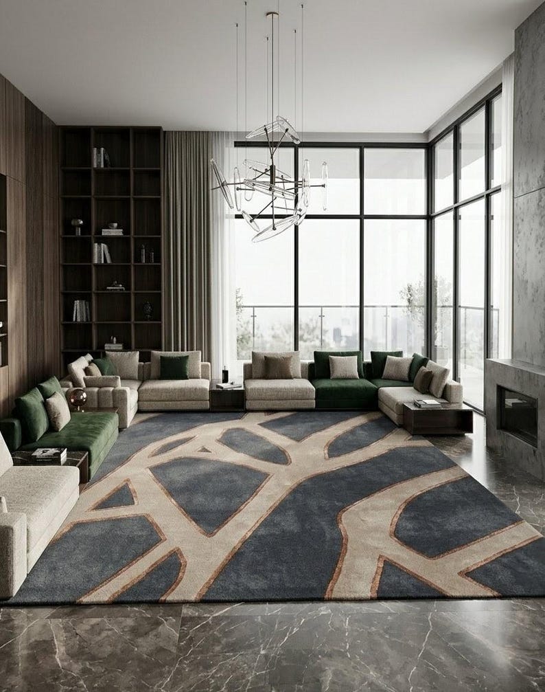 May include: A modern living room featuring a large area rug with a blue and beige abstract design. The room includes multiple beige and green sectionals, a dark wood bookshelf, and a large window with a view.