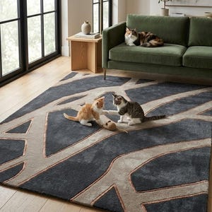 May include: A dark gray area rug with a geometric design in light gray and copper tones. Two kittens play with a toy mouse on the rug, while a calico cat rests on a green sofa. The room has a modern aesthetic with natural light.