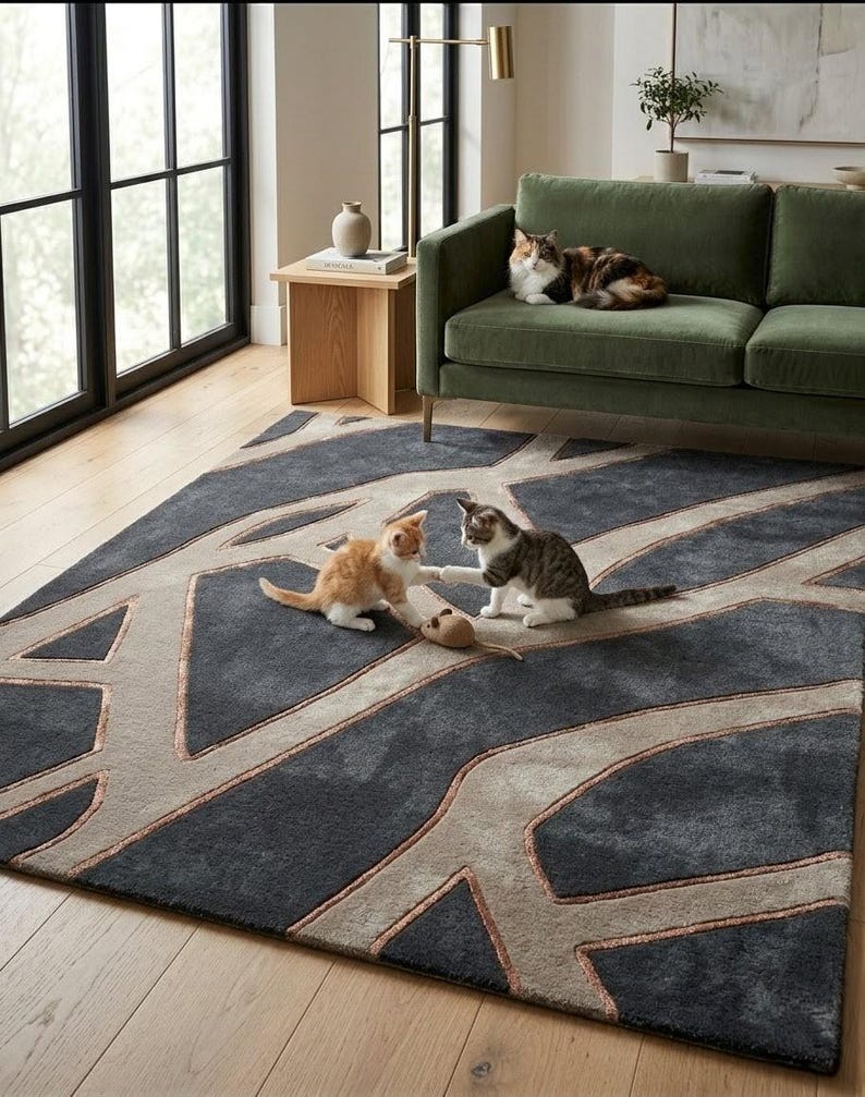 May include: A dark gray area rug with a geometric design in light gray and copper tones. Two kittens play with a toy mouse on the rug, while a calico cat rests on a green sofa. The room has a modern aesthetic with natural light.