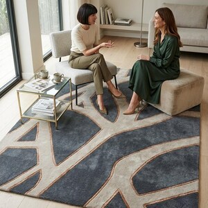 May include: A large, rectangular area rug with a modern design. The rug features a dark gray background with a light beige, tree-like pattern outlined in a copper color. The rug is placed in a living room setting.
