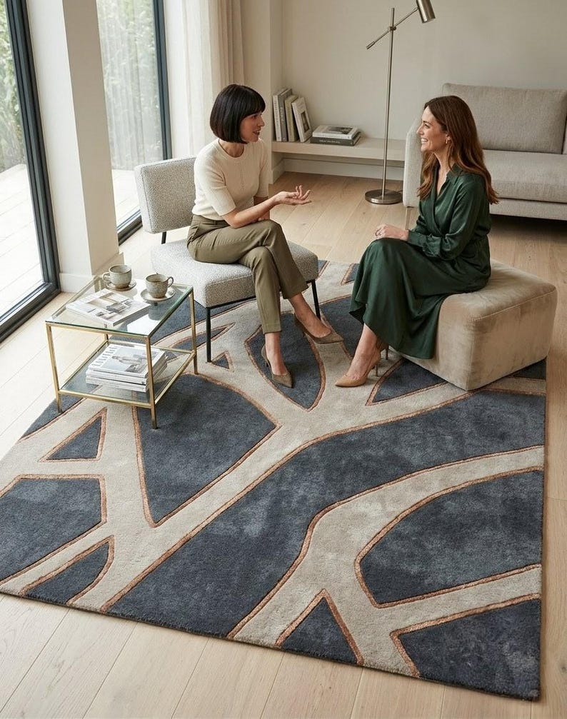 May include: A large, rectangular area rug with a modern design. The rug features a dark gray background with a light beige, tree-like pattern outlined in a copper color. The rug is placed in a living room setting.