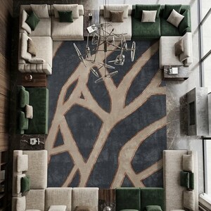 May include: An overhead view of a modern living room with multiple sectional sofas in cream and green. A large, patterned rug in navy and beige dominates the center. A unique chandelier hangs from the ceiling, and a large window is visible.