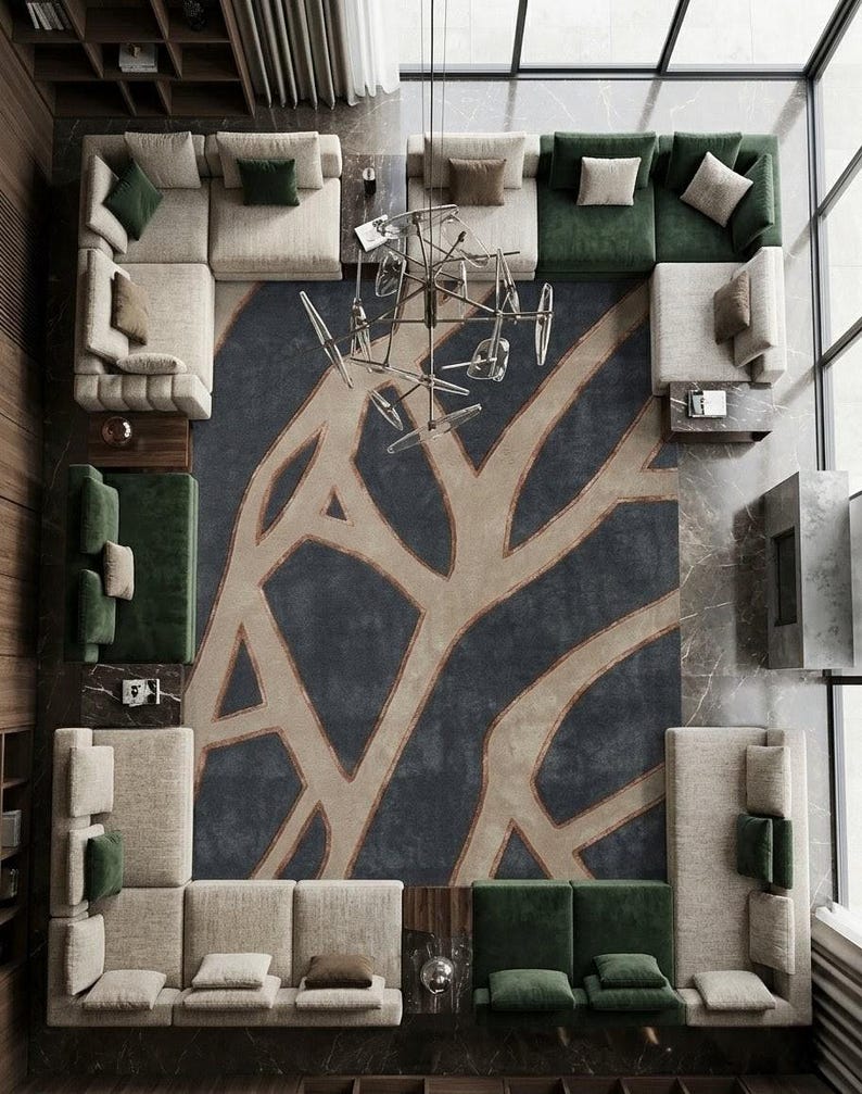May include: An overhead view of a modern living room with multiple sectional sofas in cream and green. A large, patterned rug in navy and beige dominates the center. A unique chandelier hangs from the ceiling, and a large window is visible.