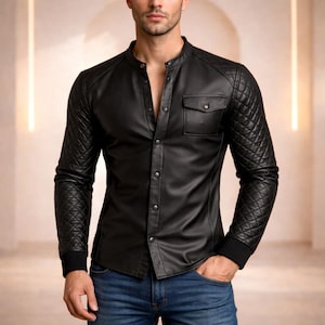 May include: Black leather shirt with quilted shoulder and sleeve detailing, a small chest pocket, and a band collar. The shirt has a button-down front and is paired with blue jeans.
