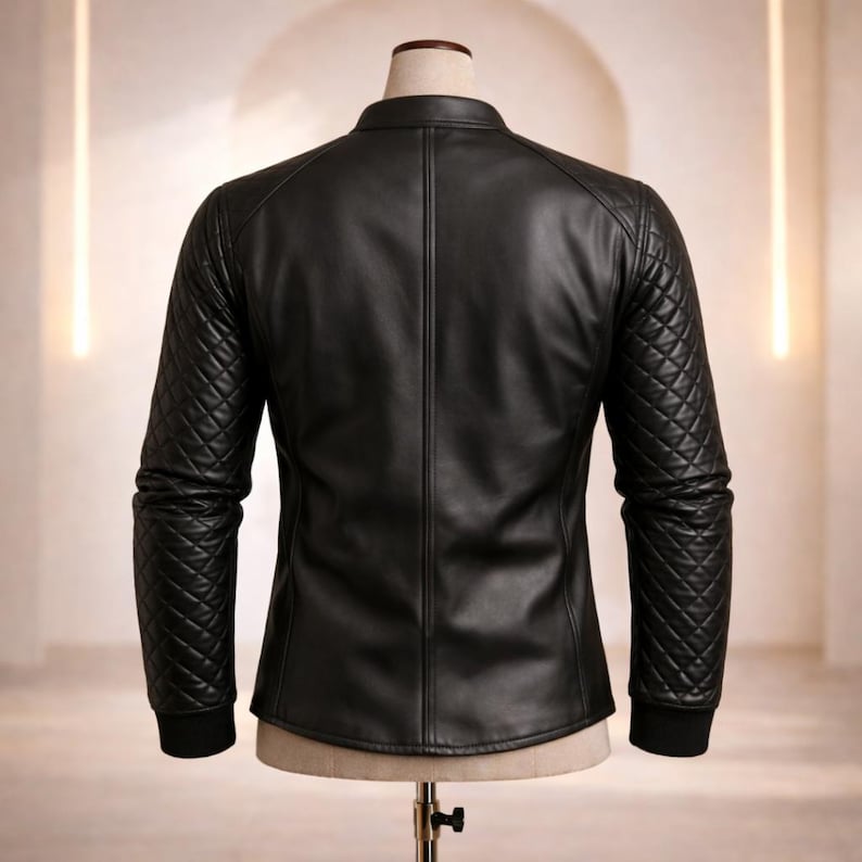 May include: Black leather jacket with quilted shoulder and sleeve detailing. The jacket has a stand-up collar and a tailored fit. The sleeves end with a black ribbed cuff. The jacket is displayed on a mannequin.