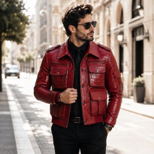 Peut inclure: Une veste en cuir rouge vif avec un motif texturé en peau de crocodile, un col classique, des épaulettes sur les épaules et quatre grandes poches avant avec fermetures à boutons. La veste est portée sur une chemise et un pantalon noirs.