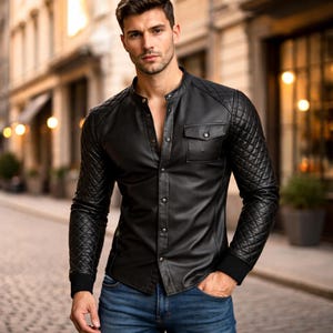 May include: Black leather shirt with quilted sleeves and a mandarin collar. The shirt has a button-down front, two chest pockets, and is paired with blue jeans. The sleeves have a quilted pattern, and the cuffs are black.