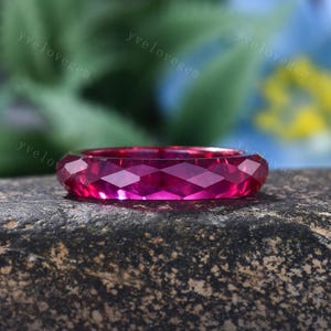 May include: A vibrant, deep pink ring featuring a faceted, geometric surface design. The band is crafted from a translucent, jewel-toned material that catches the light, creating sharp, angular reflections across its entire circular circumference.