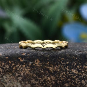 May include: A gold ring featuring a continuous wavy or scalloped band design. The metal has a polished finish that reflects light along the curved edges of the band. The text yvelovegem is visible multiple times across the image background.