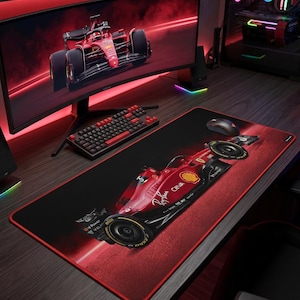 May include: A rectangular desk mat featuring a red and black Formula 1 race car graphic with yellow accents. The mat has a black surface with a red border and includes printed logos such as Ray-Ban, CEVA, and Shell on the car body.