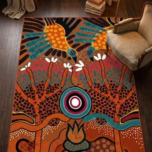 Puede incluir: Una alfombra rectangular con un vibrante diseño de puntos que presenta dos aves estilizadas en naranja y turquesa, dos árboles grandes con flores blancas, un motivo circular central y un pequeño elemento de fuego sobre fondo naranja.