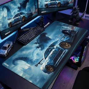 May include: A large rectangular desk mat featuring a blue-toned graphic of a sports car and a giant monster silhouette against a city skyline. The mat has a smooth surface with a black border and the text ziqou printed in the bottom left corner.