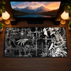 以下が含まれることがあります： 黒い背景に複雑な白い線画が描かれた長方形のデスクマット。骸骨の姿、装飾的な十字架のモチーフ、手のイラストが含まれています。テキストには「orphic (adj) mysterious and entrancing beyond ordinary understanding」と書かれています。