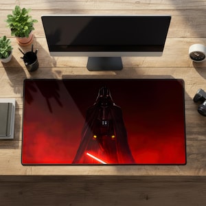 Könnte beinhalten: Rechteckige Schreibtischunterlage mit Darth Vader aus Star Wars, vor rotem Hintergrund. Die Matte hat einen schwarzen Rand und liegt auf einem Holzschreibtisch, mit einem Computermonitor, Pflanzen und anderem Büromaterial.