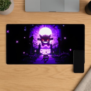 May include: A rectangular desk mat with a purple and black illustration of a Gengar character in front of a full moon. The design includes a graveyard scene with a gate and cross symbols. A black smartphone is on the right.
