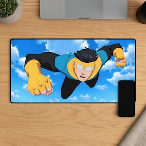 May include: A rectangular desk mat featuring a graphic illustration of a flying superhero with black hair, wearing a blue and yellow suit with black sleeves and gloves, soaring through a bright blue sky filled with white clouds.