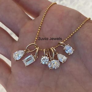 May include: A gold necklace featuring several diamond pendants in different shapes, such as pear, emerald, and oval. The necklace is suspended from a fine chain. The text "Zuvia Jewels" is displayed.