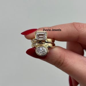 Puede incluir: Tres anillos de oro con piedras preciosas transparentes. El anillo superior tiene una piedra rectangular, el anillo central es liso y el anillo inferior tiene una piedra ovalada. El texto "Zuvia Jewels" es visible.