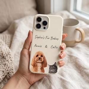 K&ouml;nnte beinhalten: Eine cremefarbene Smartphone-H&uuml;lle mit einer individuellen Illustration eines braunen Spaniels und einer grauen getigerten Katze. Der Text "Sophie's Fur Babies" und "Annie & Callie" ist in schwarzer Schrift &uuml;ber den Tierportr&auml;ts gedruckt.