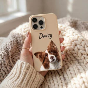 K&ouml;nnte beinhalten: Eine beige Smartphone-H&uuml;lle mit einer individuellen Illustration eines braun-wei&szlig;en Hundes und dem Namen Daisy in dunkelgrauer Schreibschrift dar&uuml;ber. Die H&uuml;lle verf&uuml;gt &uuml;ber eine Aussparung f&uuml;r ein Dreifach-Kamerasystem an der oberen Ecke.