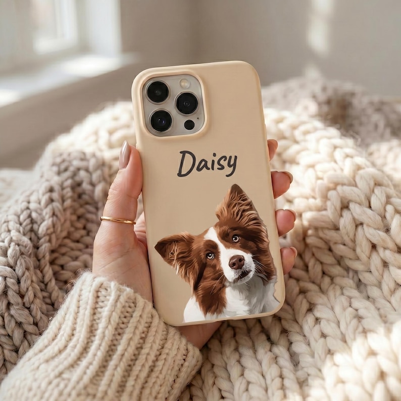 K&ouml;nnte beinhalten: Eine beige Smartphone-H&uuml;lle mit einer individuellen Illustration eines braun-wei&szlig;en Hundes und dem Namen Daisy in dunkelgrauer Schreibschrift dar&uuml;ber. Die H&uuml;lle verf&uuml;gt &uuml;ber eine Aussparung f&uuml;r ein Dreifach-Kamerasystem an der oberen Ecke.