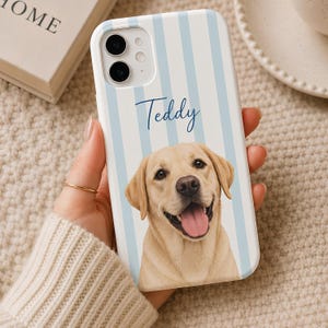 May include: A white smartphone case featuring vertical light blue stripes and a portrait of a yellow Labrador retriever with its tongue out. The name Teddy is printed in dark blue script above the dog's head. The case has a dual camera cutout.