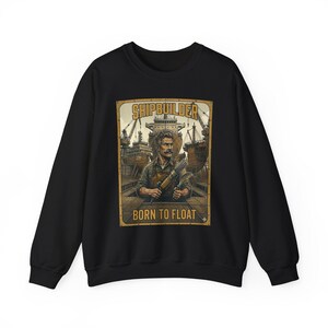 May include: Black sweatshirt featuring a vintage-style illustration of a shipbuilder holding tools, with the words "SHIPBUILDER" and "BORN TO FLOAT" in a rectangular frame. The design includes a ship and shipyard background.