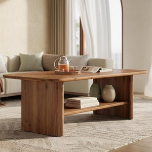 May include: A rectangular wooden coffee table with a lower shelf, holding books and decorative vases. A glass teapot and tray sit on top. The table is in a living room with a sofa and rug.