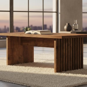 May include: A rectangular wooden coffee table with a warm brown finish. The table has a slatted design on one side and is placed on a beige rug. A book and a mug are on the table. The table is 60 inches long and 30 inches wide.