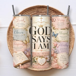 May include: Three cylindrical tumblers with black straws featuring a cream and pastel floral background. The design includes the text GOD SAYS I AM, along with religious phrases like Loved, Chosen, Forgiven, Strong, Blessed, and Worthy, accompanied by butterflies, a crown, and an open book illustration.