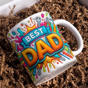 May include: White ceramic mug with the words "BEST DAD" in orange and yellow, surrounded by colorful paint splatters and tools. The mug has a white handle and is nestled in brown packing material.