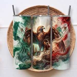 Puede incluir: Un vaso cilíndrico de acero inoxidable con un diseño envolvente de un águila real posada sobre un cactus, rodeada de humo arremolinado en tonos verde, blanco y rojo, junto a la bandera de México con su emblema central y una pajita negra.