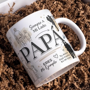 Puede incluir: Taza de cerámica blanca con la palabra "PAPA" en letras negras grandes. La taza presenta ilustraciones de un padre y un niño, junto con texto en español. La taza se presenta en una caja de regalo con relleno de papel marrón.
