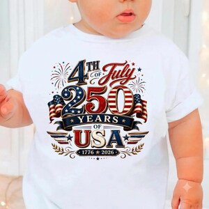 May include: A white t-shirt featuring a graphic design with the text 4th of July 250 Years of USA 1776-2026. The design includes red, white, and blue colors, American flag patterns, star motifs, and firework illustrations centered on the chest.