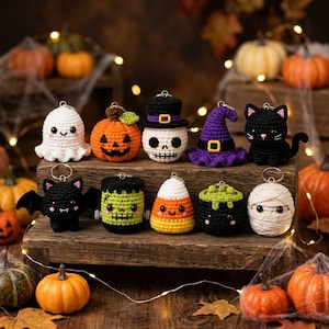 May include: A collection of ten small, crocheted Halloween-themed keychains arranged on a wooden block. The figures include a white ghost, orange pumpkin, skull with a top hat, purple witch hat, black cat, bat, Frankenstein, candy corn, cauldron, and mummy.